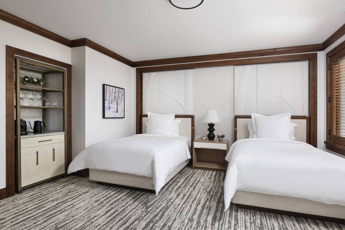 A hotel room with two beds, a minibar, a large window with a view, and a wooden ceiling.