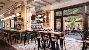A restaurant with a bar area, outdoor seating, and large windows offering a view of the outdoors. - Four Seasons Resort Jackson Hole (Teton Village)