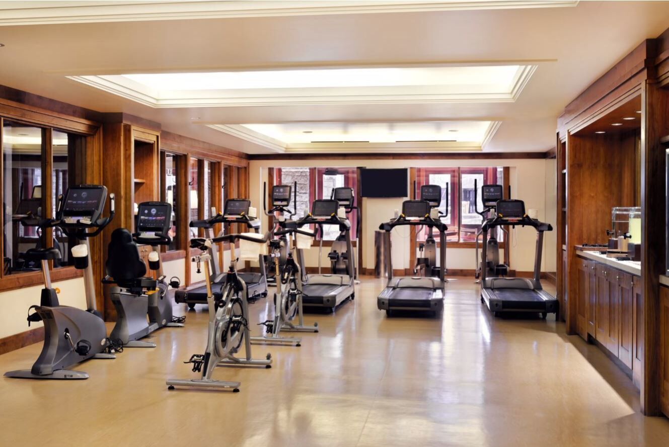 Academia com diversos equipamentos de cardio, painéis de madeira e um grande espelho.