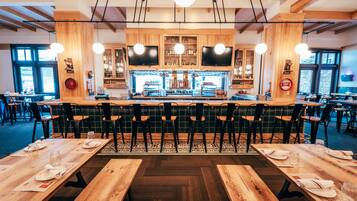 A restaurant with wooden tables and chairs, a bar area, and large windows.