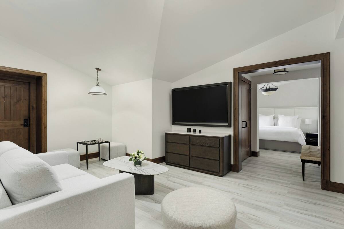A modern hotel room with a large bed, a flat-screen TV, a sofa, a coffee table, and a small side table.