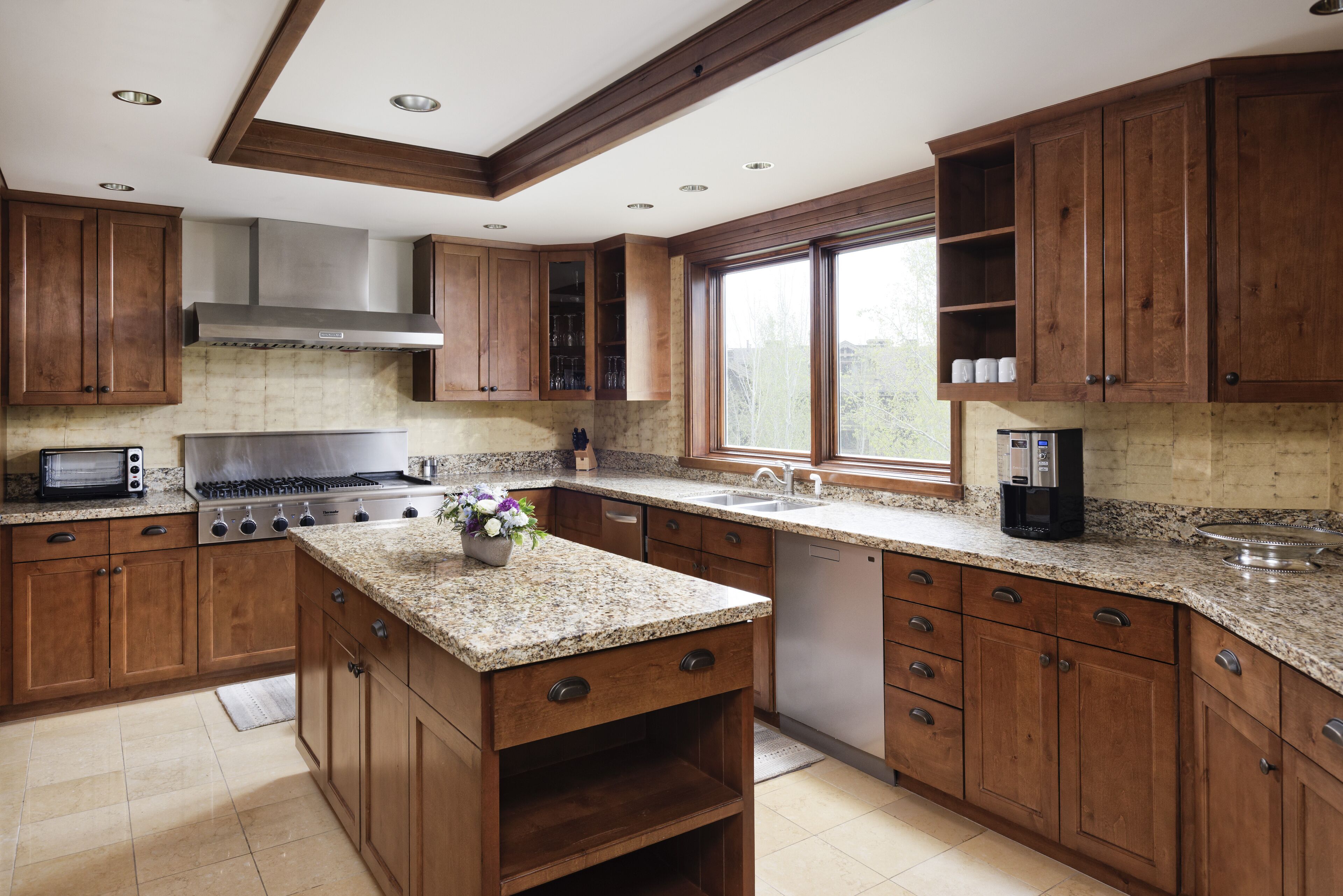 A kitchen with wooden cabinets, granite countertops, a stove, and a window providing natural light.