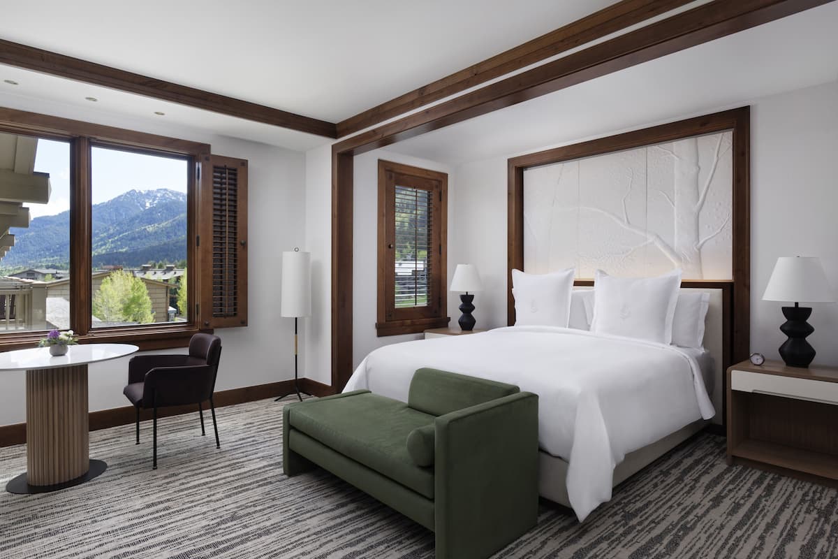 A hotel room with a large bed, a desk, a chair, and a view of mountains.
