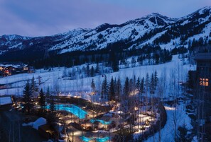 Paisaje nevado de montaña con una zona de piscina iluminada y edificios en primer plano.