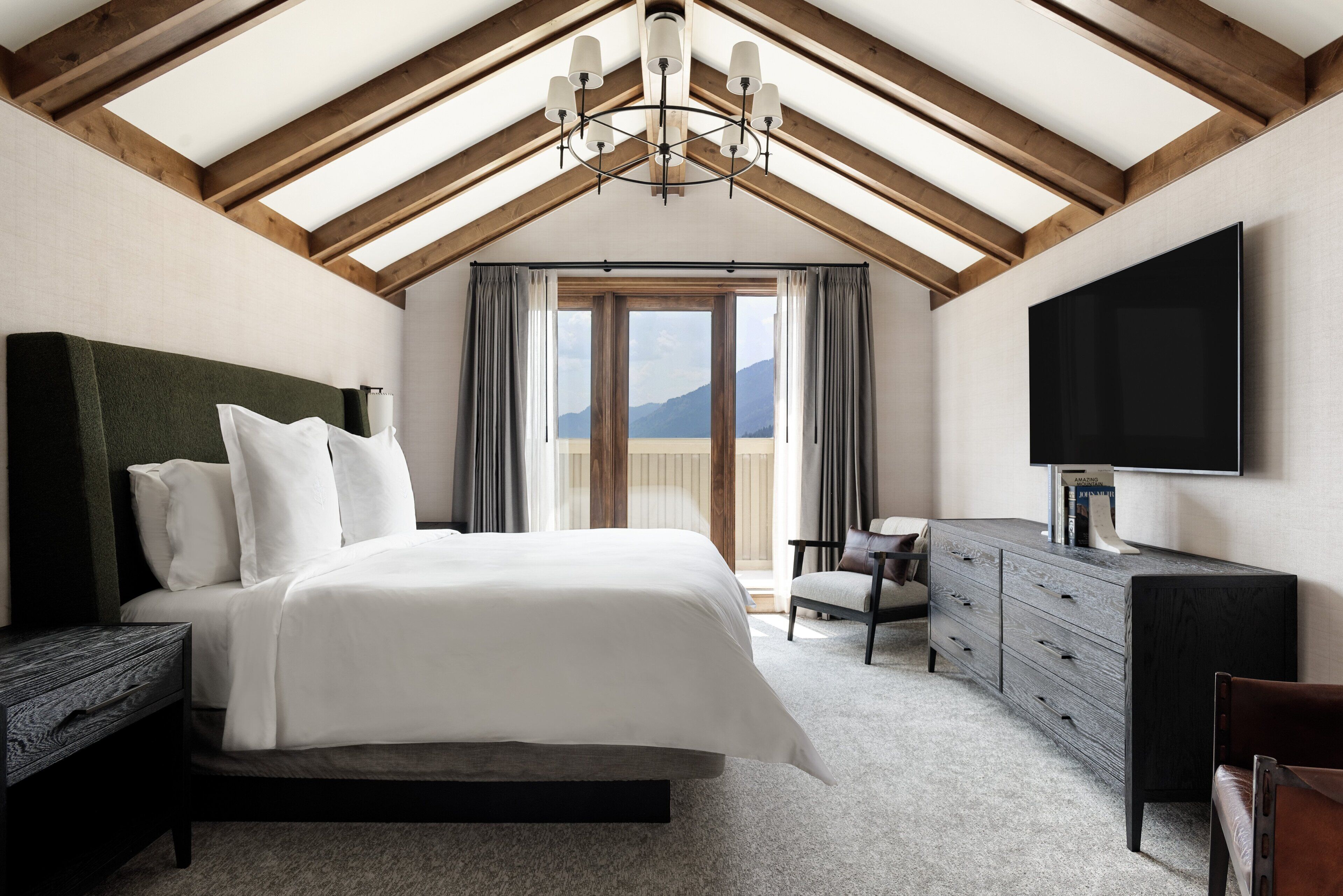 Un dormitorio con una cama grande, un aparador, un televisor y vistas a montañas a través de un ventanal.