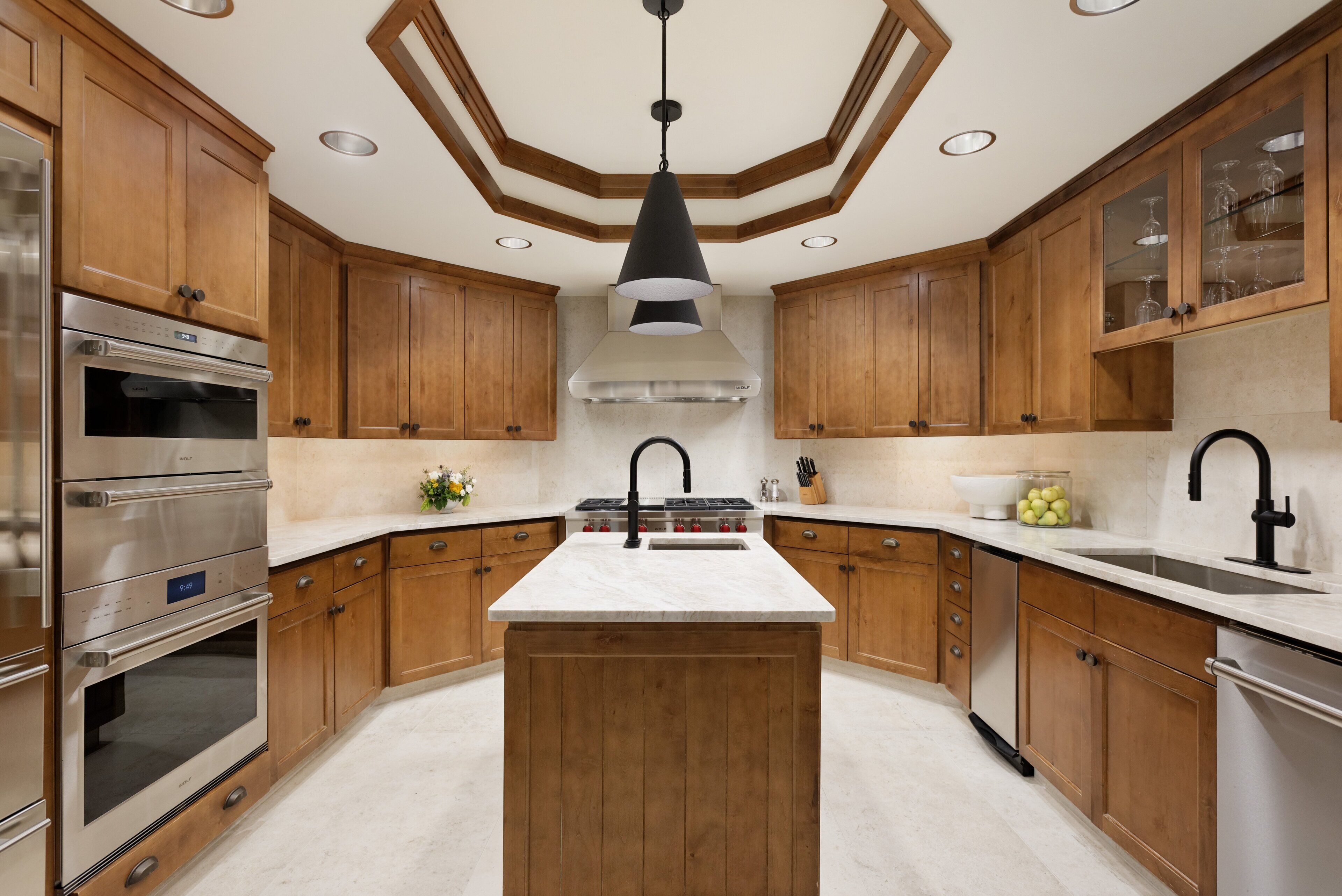 A modern kitchen with wooden cabinets, a central island, stainless steel appliances, and a black pendant light.