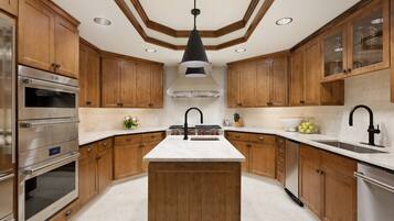 A modern kitchen with wooden cabinets, a central island, stainless steel appliances, and a black pendant light.