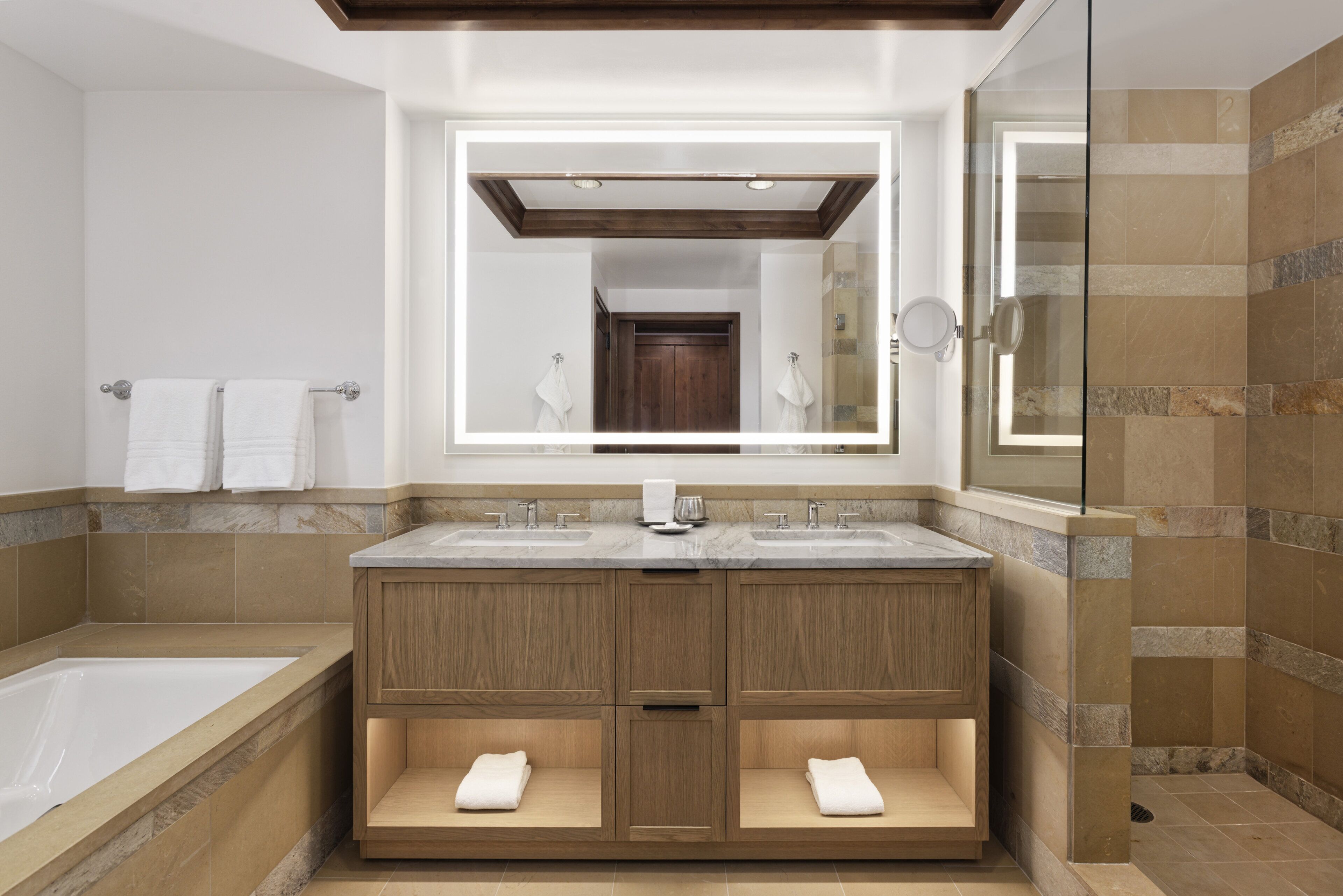 A modern bathroom with a large mirror, two sinks, a bathtub, and a shower area.