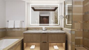 A modern bathroom with a large mirror, two sinks, a bathtub, and a shower area.