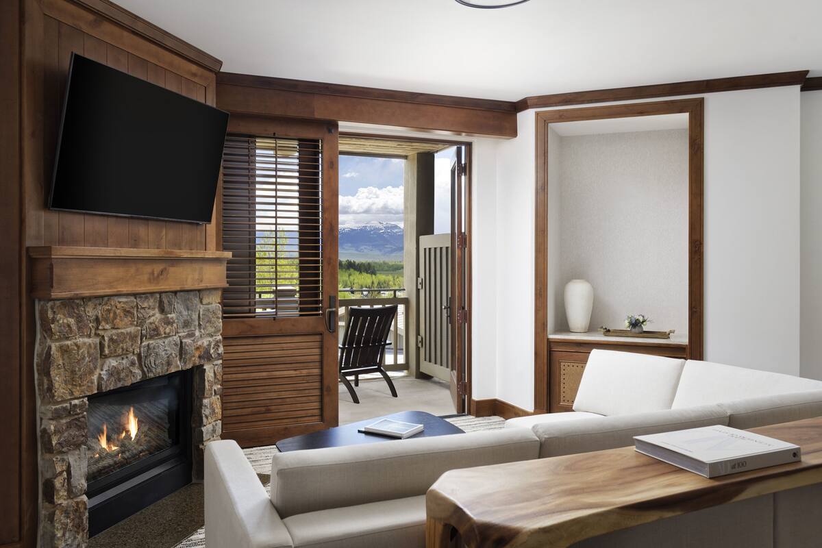A modern living room with a stone fireplace, a flat-screen TV, a sofa, and a view of mountains through an open door.