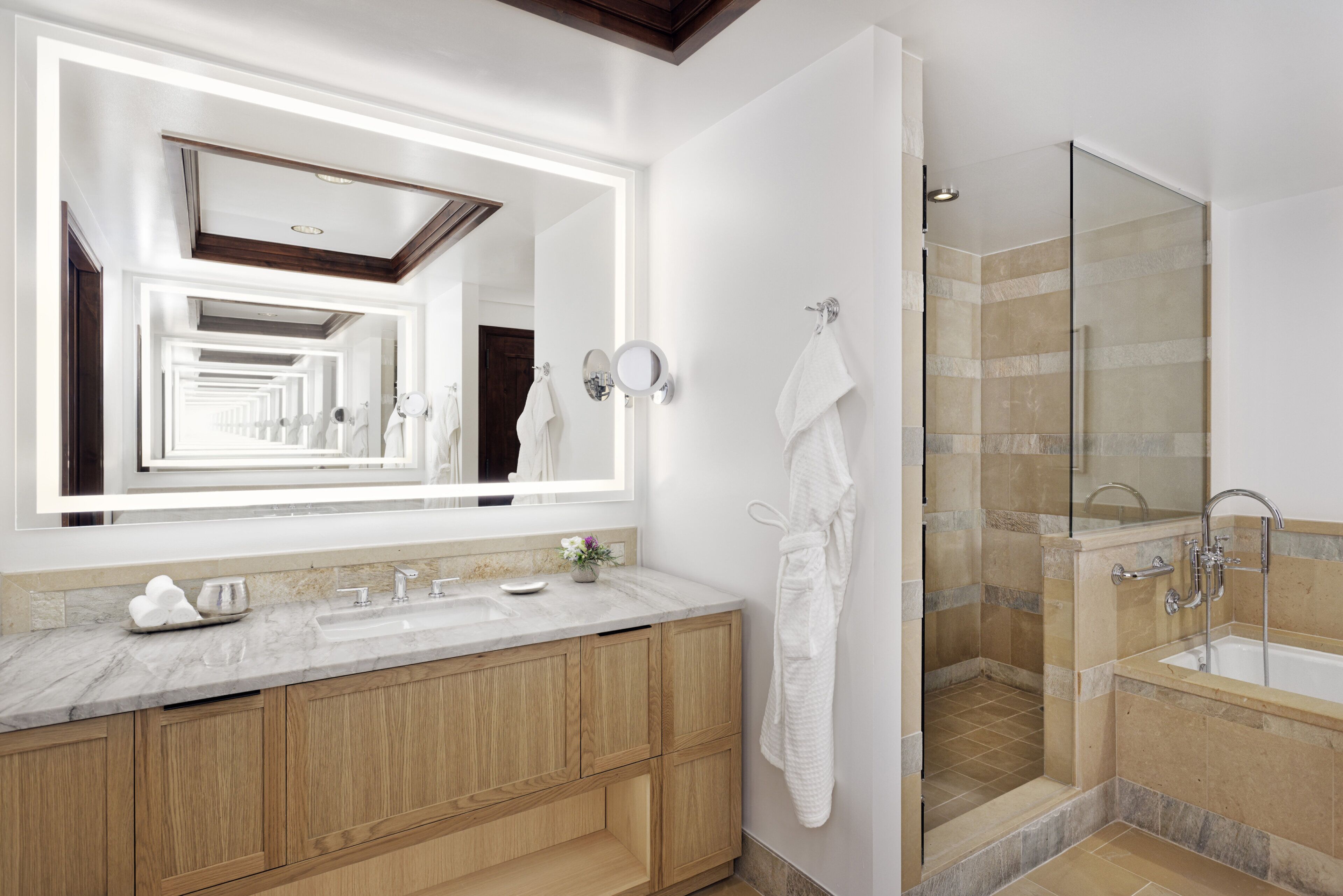A modern bathroom with a large mirror, wooden vanity, and a glass-enclosed shower area.