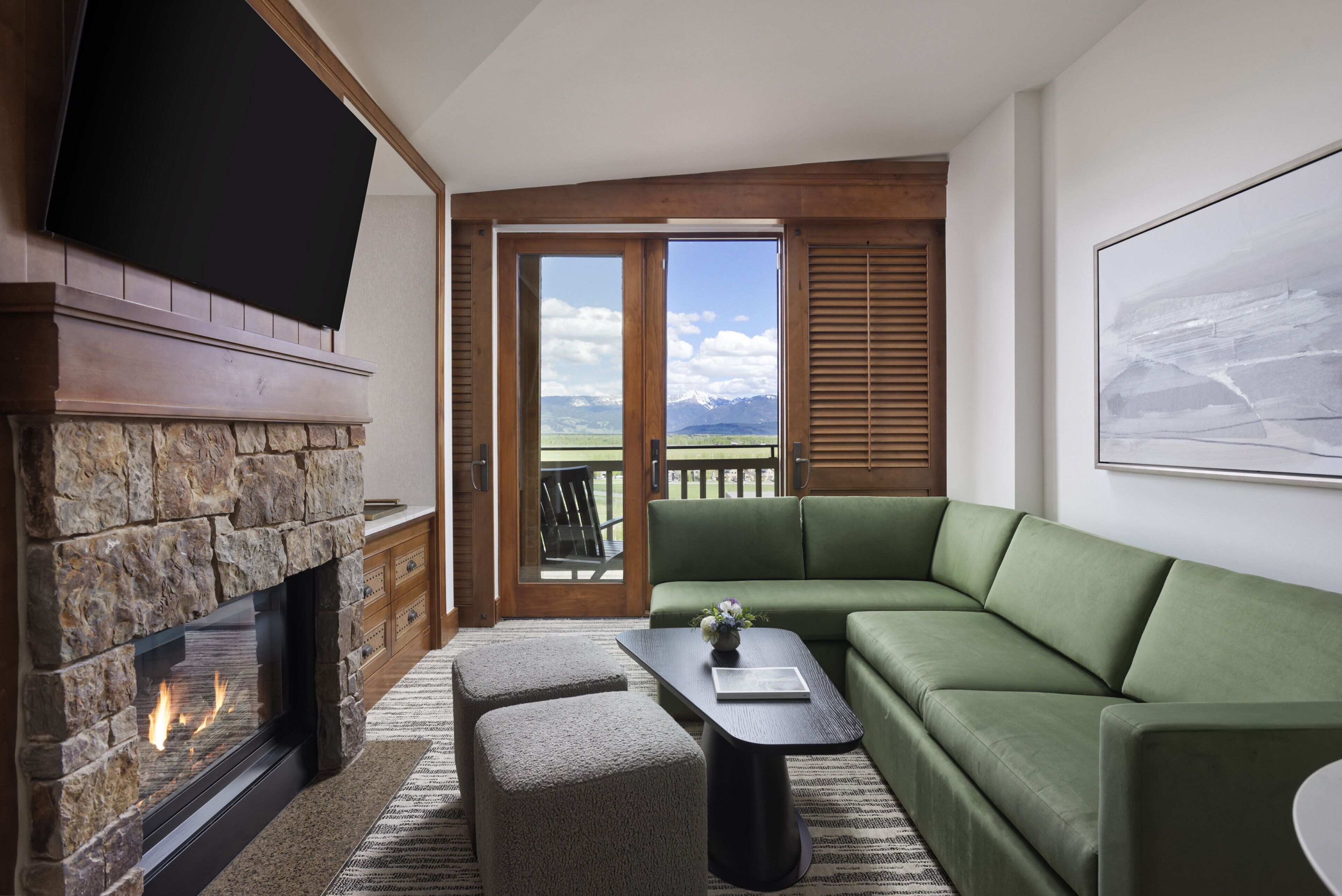 Una sala de estar moderna con chimenea de piedra, un sofá verde, una mesa de centro y un amplio ventanal con vistas a la montaña.