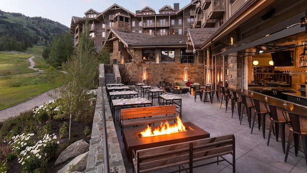 A hotel with a patio area featuring outdoor seating, a bar, and a fireplace. - Four Seasons Resort Jackson Hole (Teton Village)