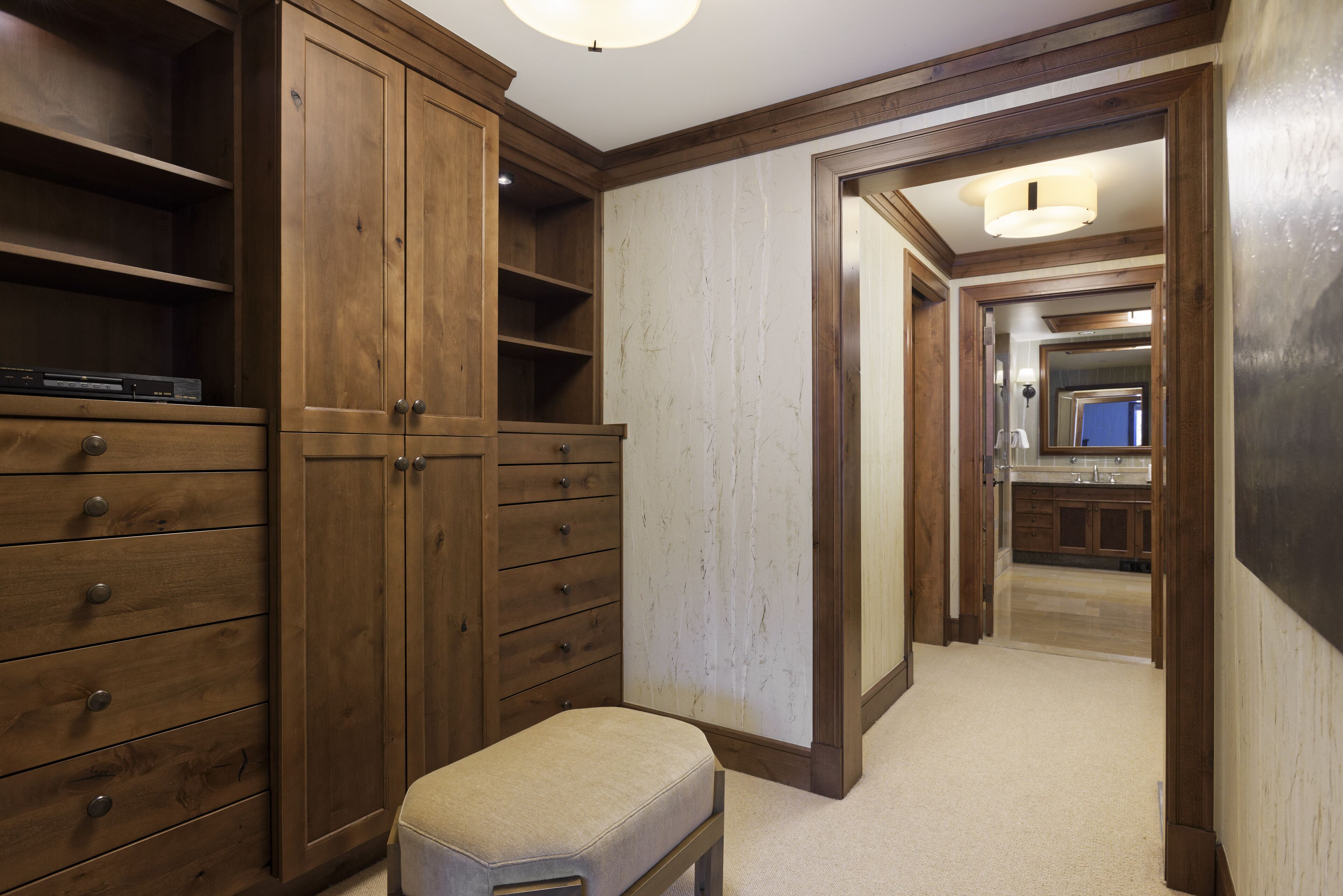 A hallway with wooden cabinets, a bench, and a view into a kitchen area.