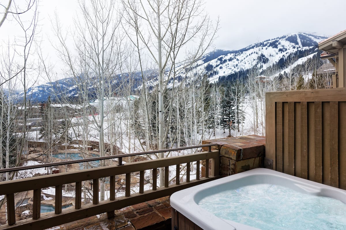 A hot tub on a wooden deck with a view of snow-covered mountains.