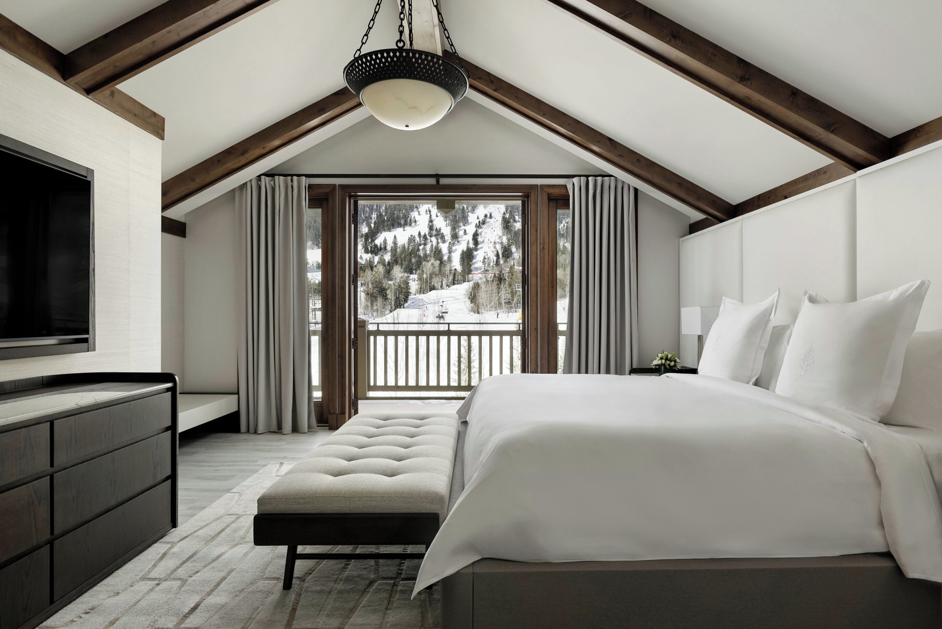 A bedroom with a large bed, a TV, and a balcony with a snowy view.