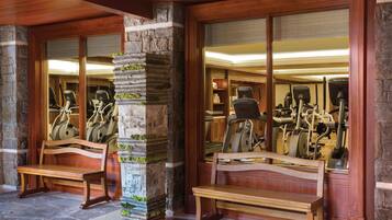 Un gimnasio con equipo de ejercicio, bancos de madera y pilares de piedra.
