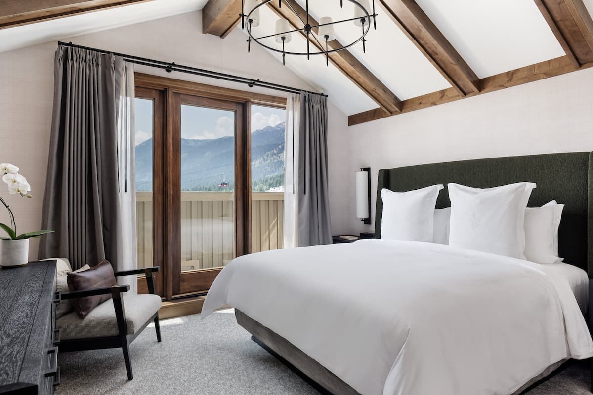 A bedroom with a large bed, a desk, a chair, and a view of mountains through the window.