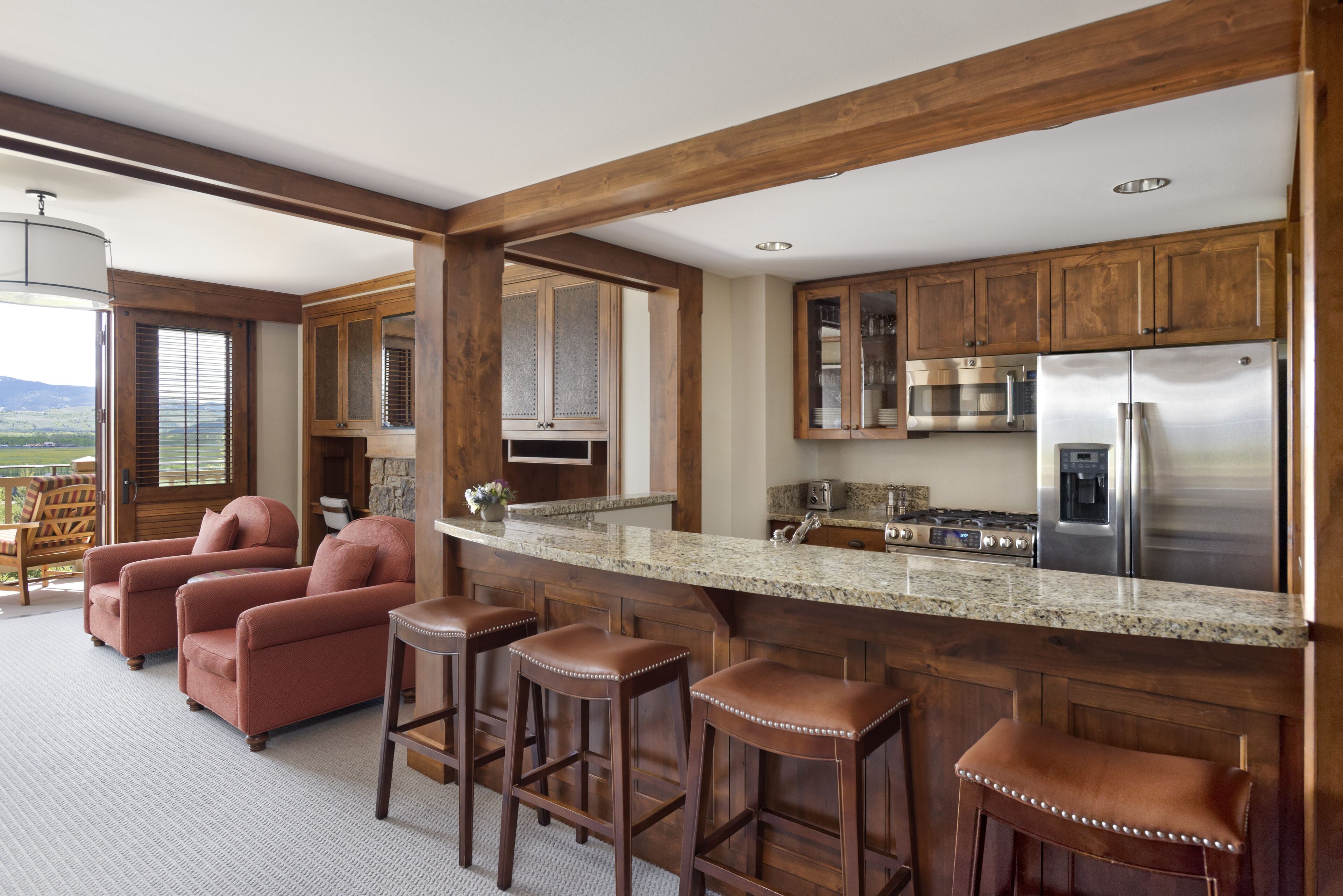 A kitchen with wooden cabinets, a stainless steel refrigerator, and a bar area with stools.