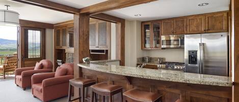 A kitchen with wooden cabinets, a stainless steel refrigerator, and a bar area with stools.