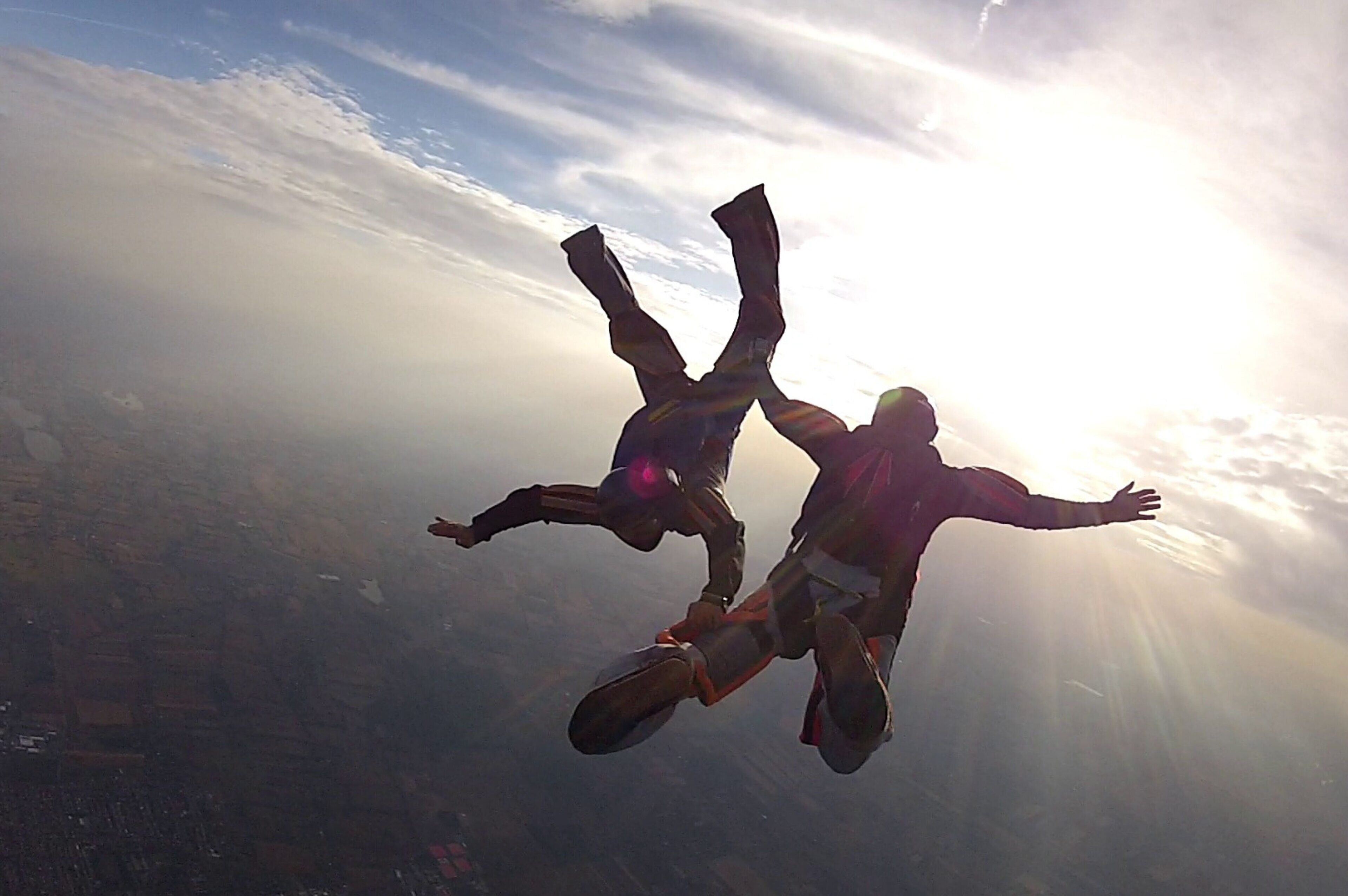 Two people skydiving with the sun shining through the clouds.