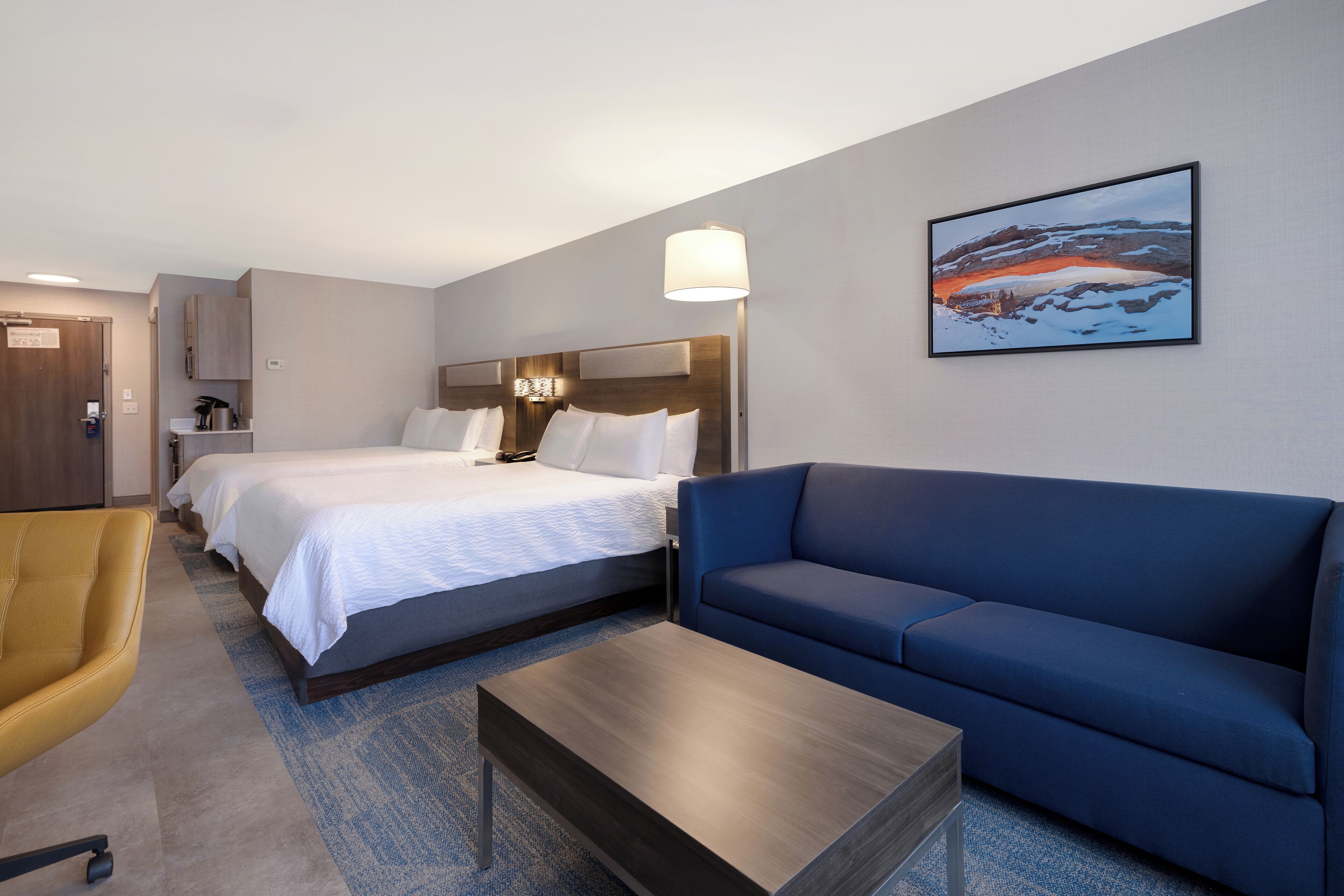 A hotel room with two beds, a blue sofa, a wooden coffee table, and a painting on the wall.