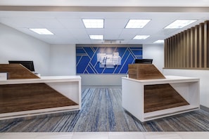 A reception area with two wooden reception desks, a blue geometric wall design, and a carpeted floor.