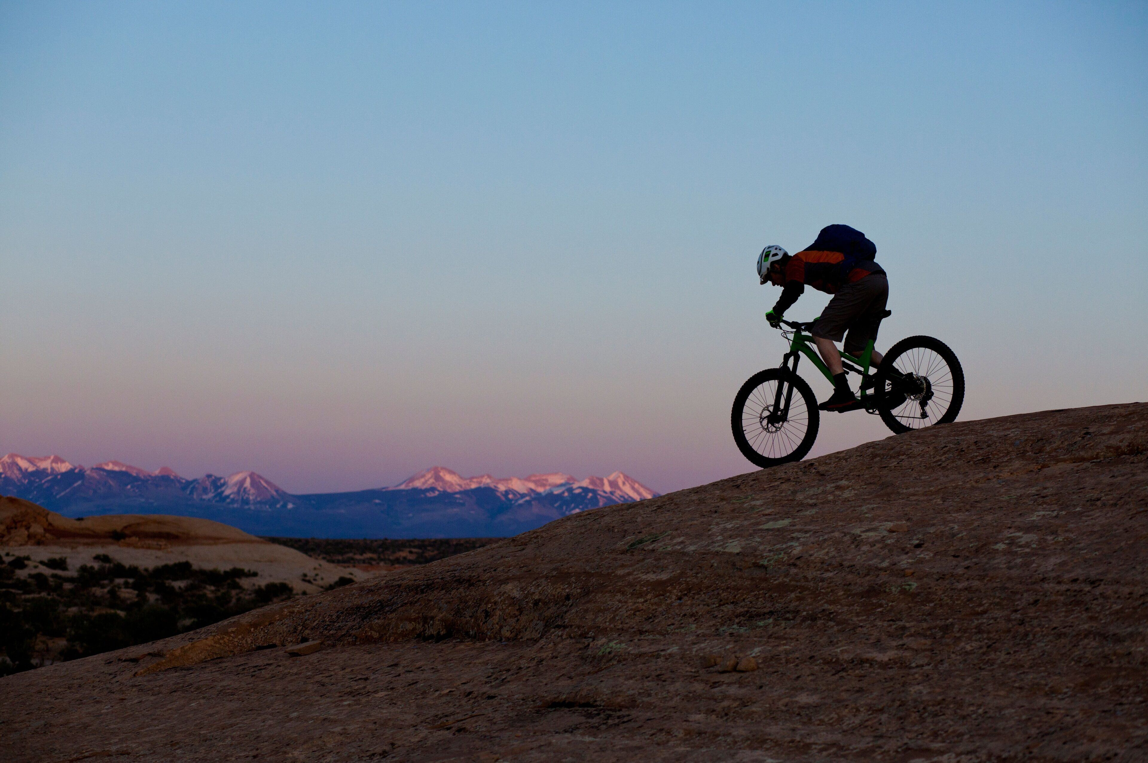 Una persona pedaleando en bicicleta de montaña por un sendero de tierra, con un paisaje montañoso de fondo.