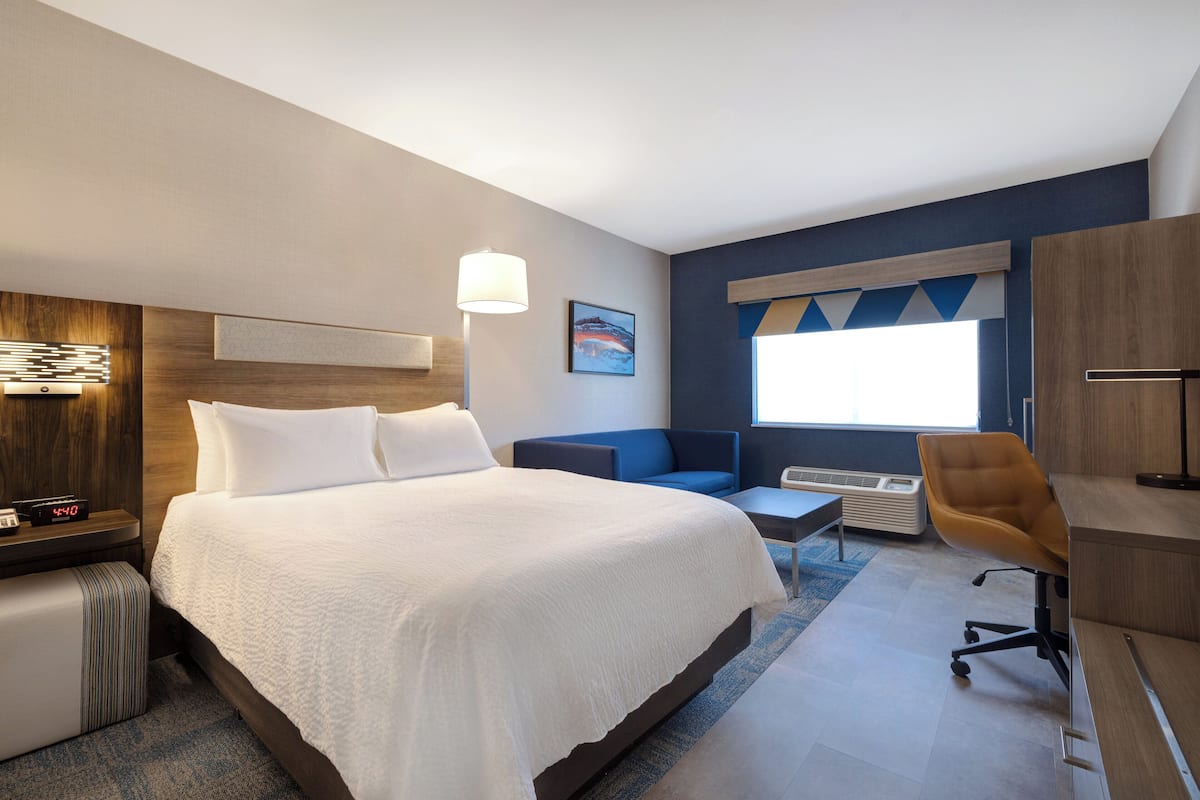 Habitación de hotel con una cama grande, un escritorio, una silla, una lámpara y una ventana con vistas.
