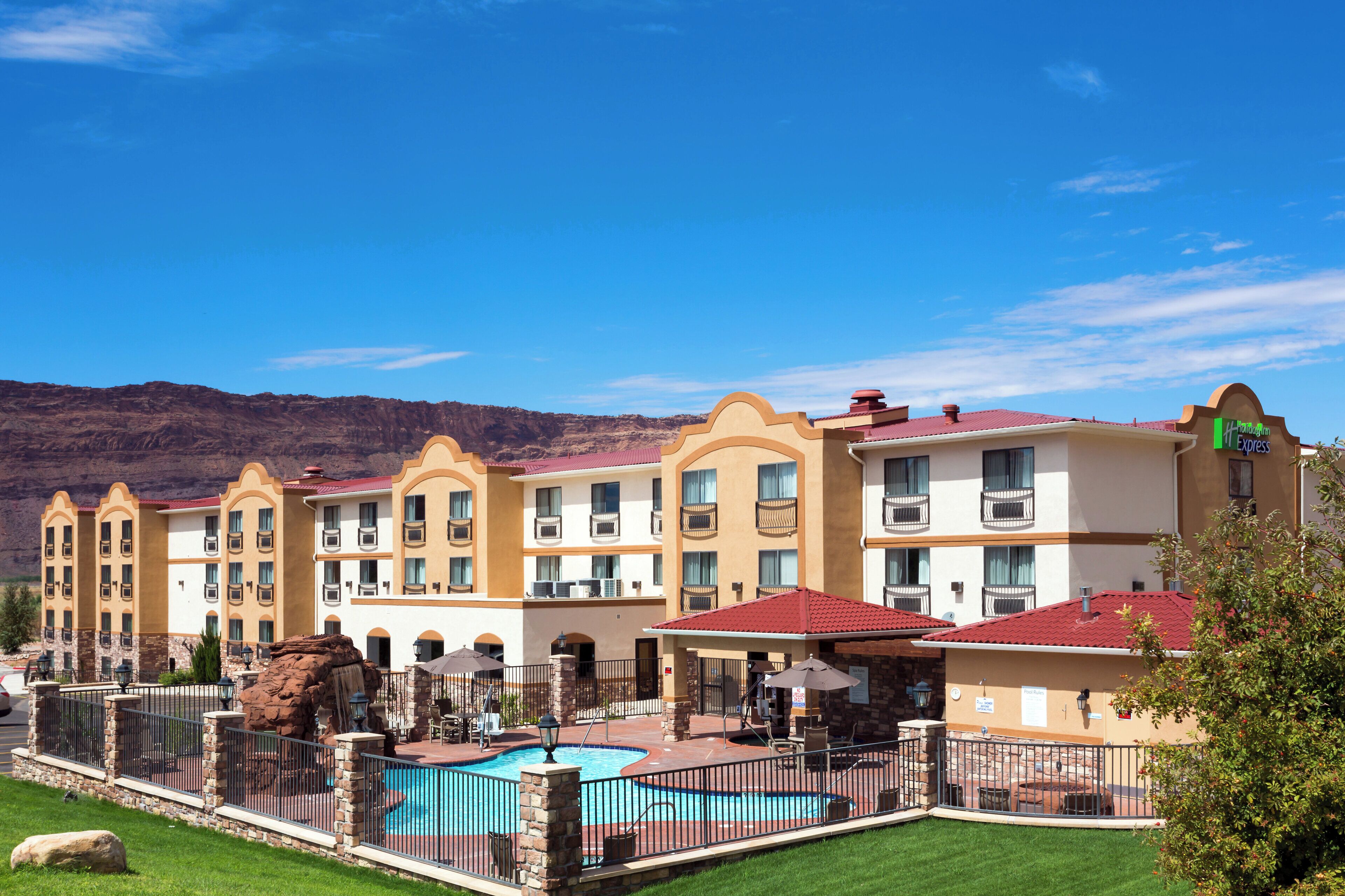 Un hotel con varios balcones, piscina y montañas al fondo.