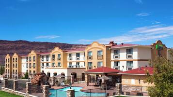 Un hotel con varios balcones, piscina y montañas al fondo.