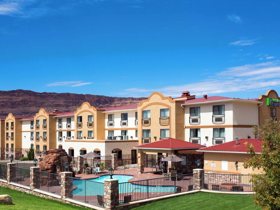 Un hotel con varios balcones, piscina y montañas al fondo.