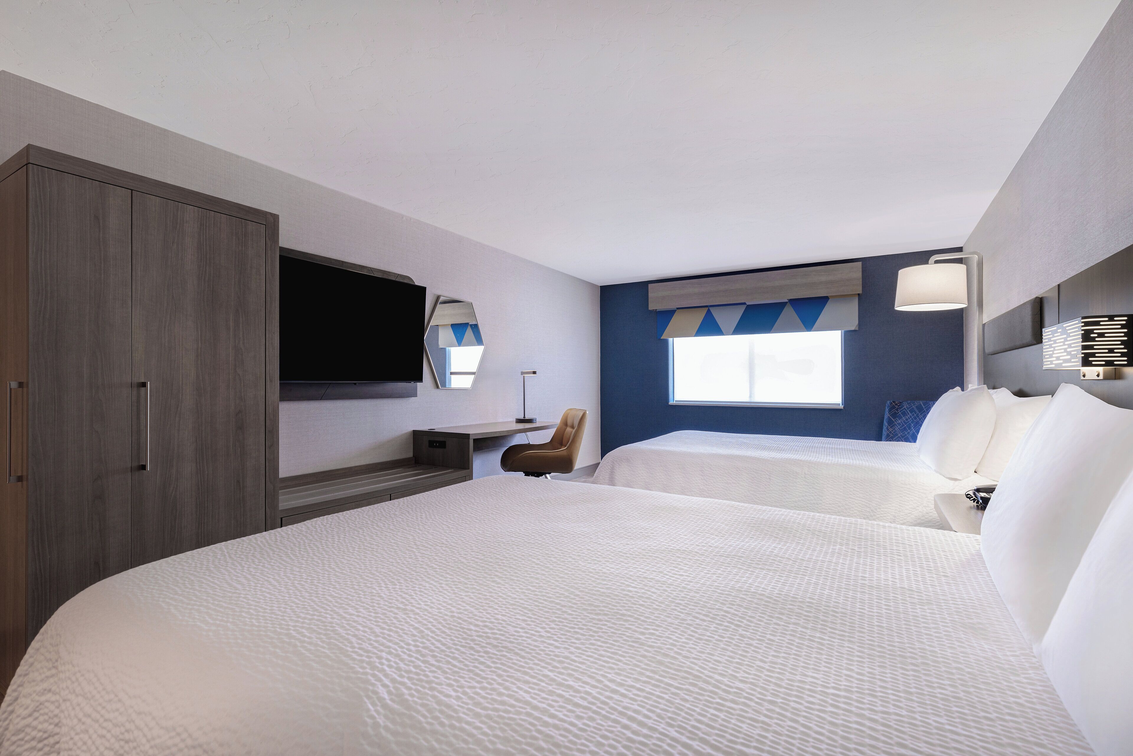 A hotel room with two beds, a desk, a chair, a television, and a window with a view.