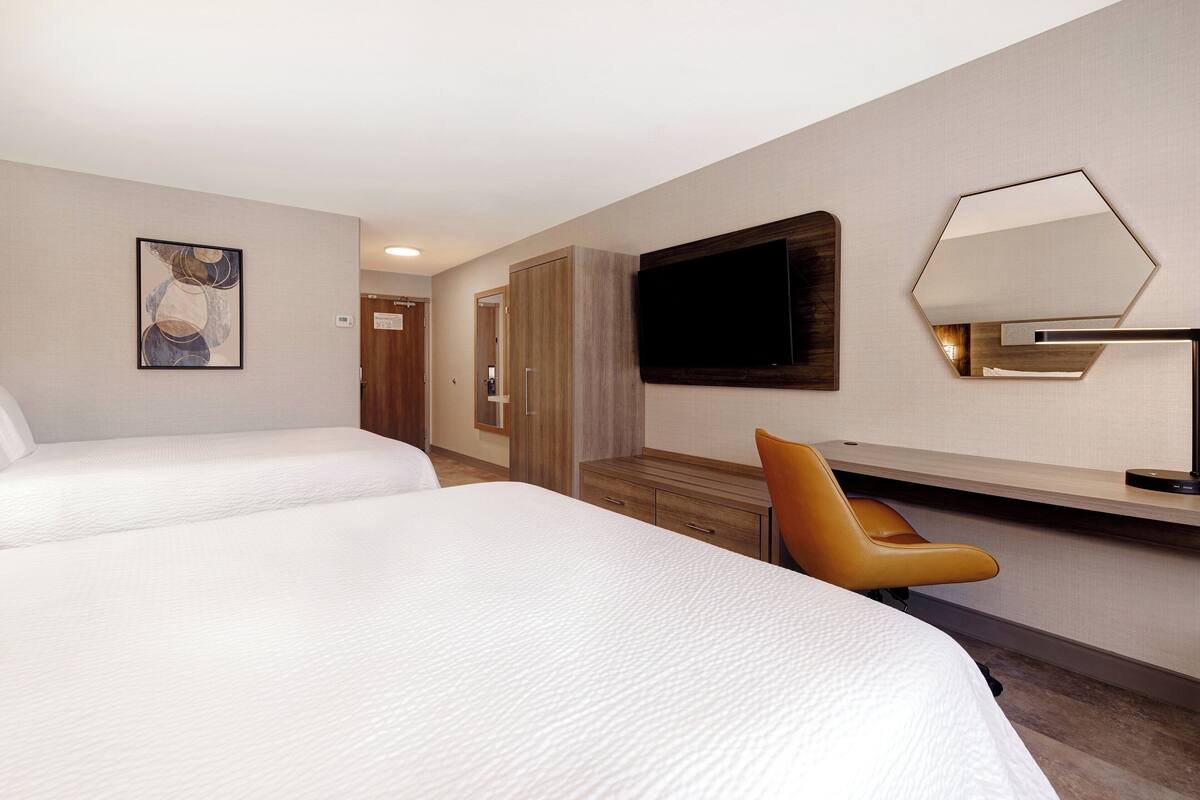 Una habitación de hotel con dos camas, un escritorio con silla, un televisor y un cuadro en la pared.