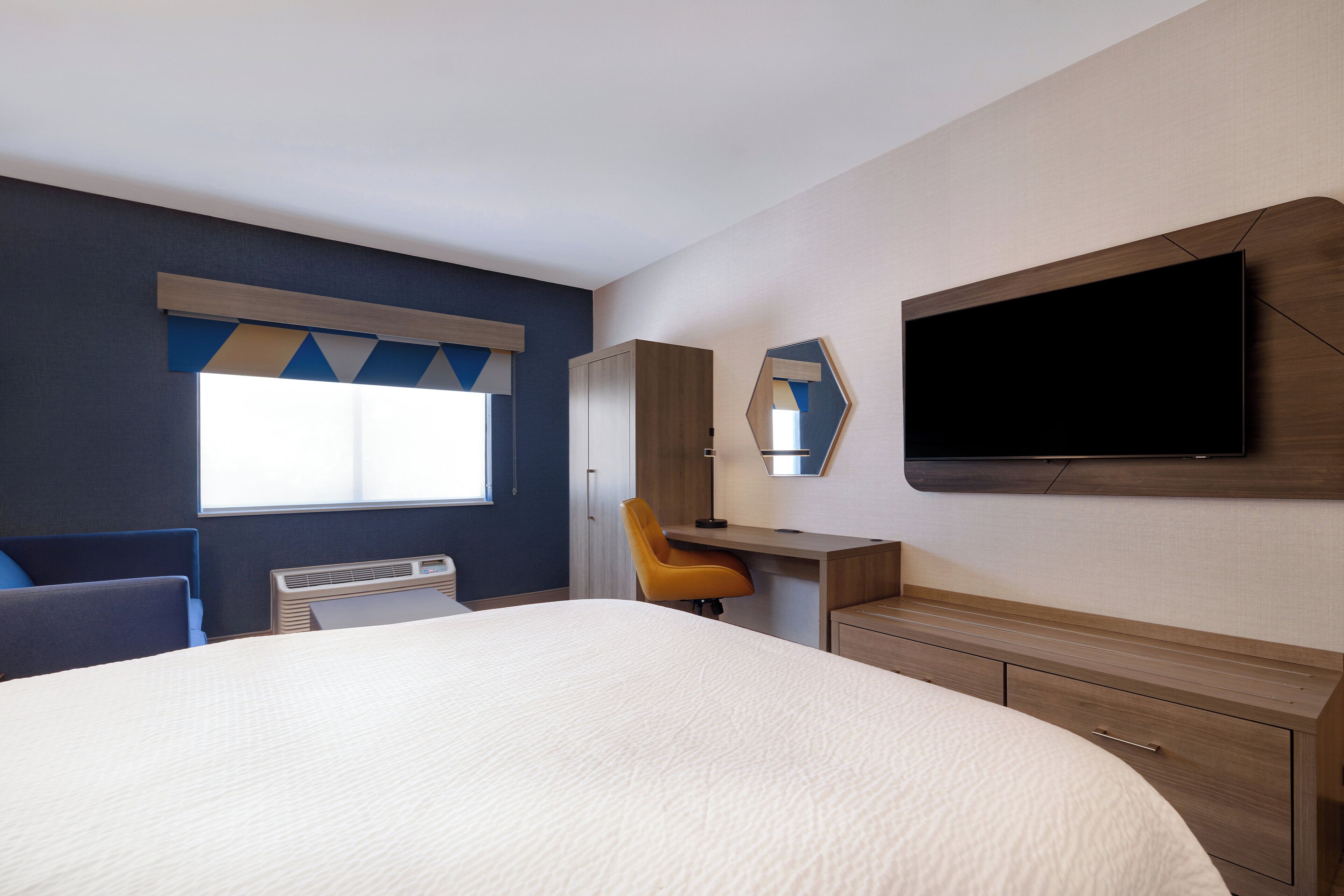 Une chambre d’hôtel comprenant un lit, un bureau, une chaise, une télévision et une armoire.