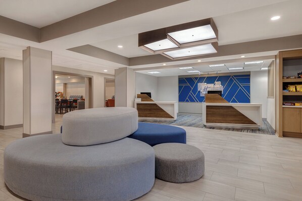 A modern lobby with a reception desk, seating area with ottomans, and a blue accent wall.