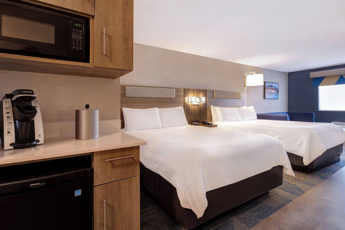 Habitación de hotel con dos camas, microondas, cafetera y refrigerador pequeño.