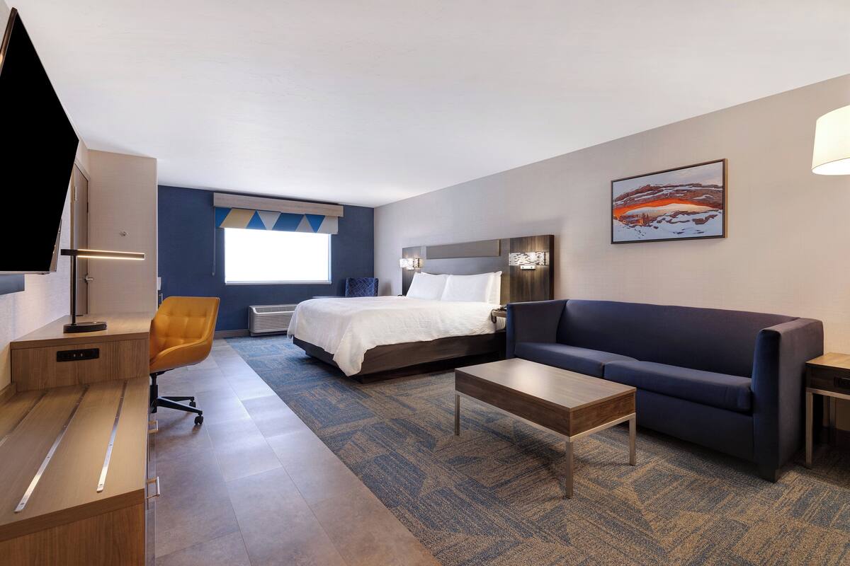 Habitación de hotel con cama, sofá, escritorio, televisor y un cuadro en la pared.