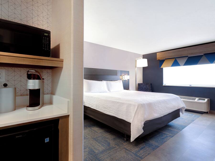 A hotel room with a bed, a microwave, a coffee maker, and a desk with a lamp.