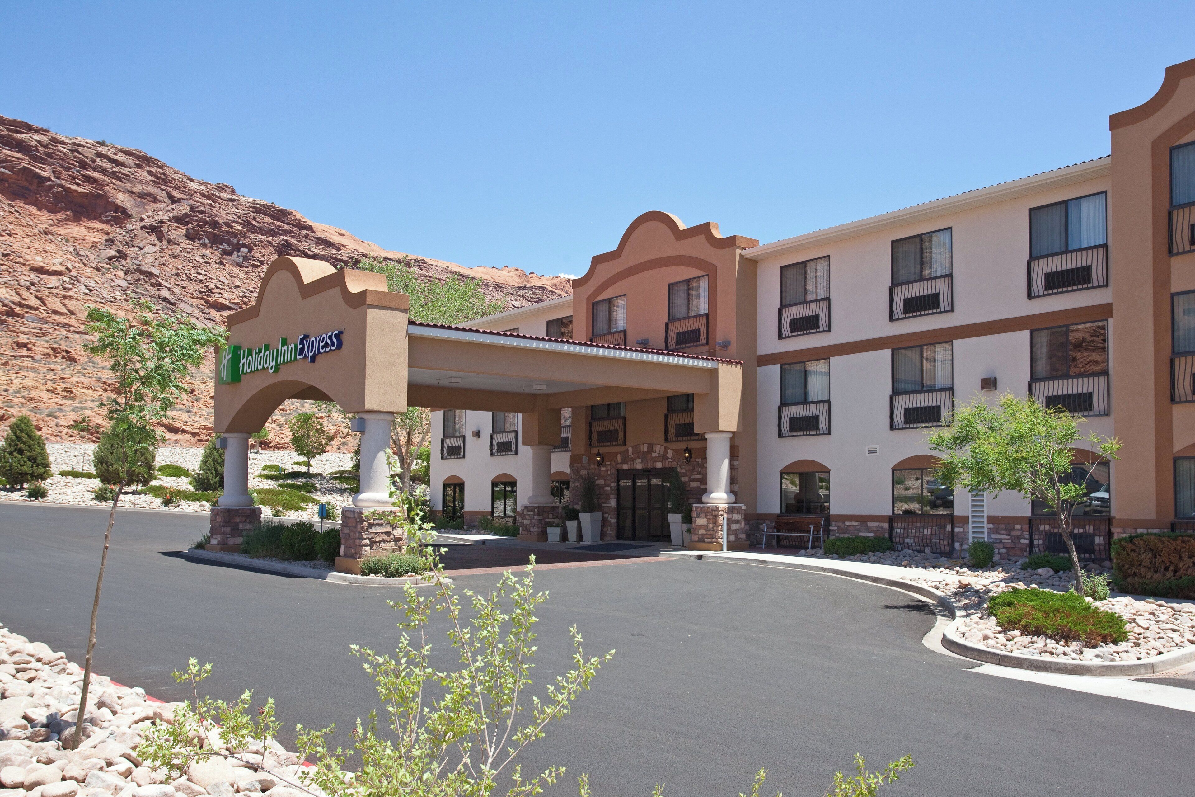 A Holiday Inn Express hotel with a covered entrance, multiple balconies, and a desert landscape in the background.