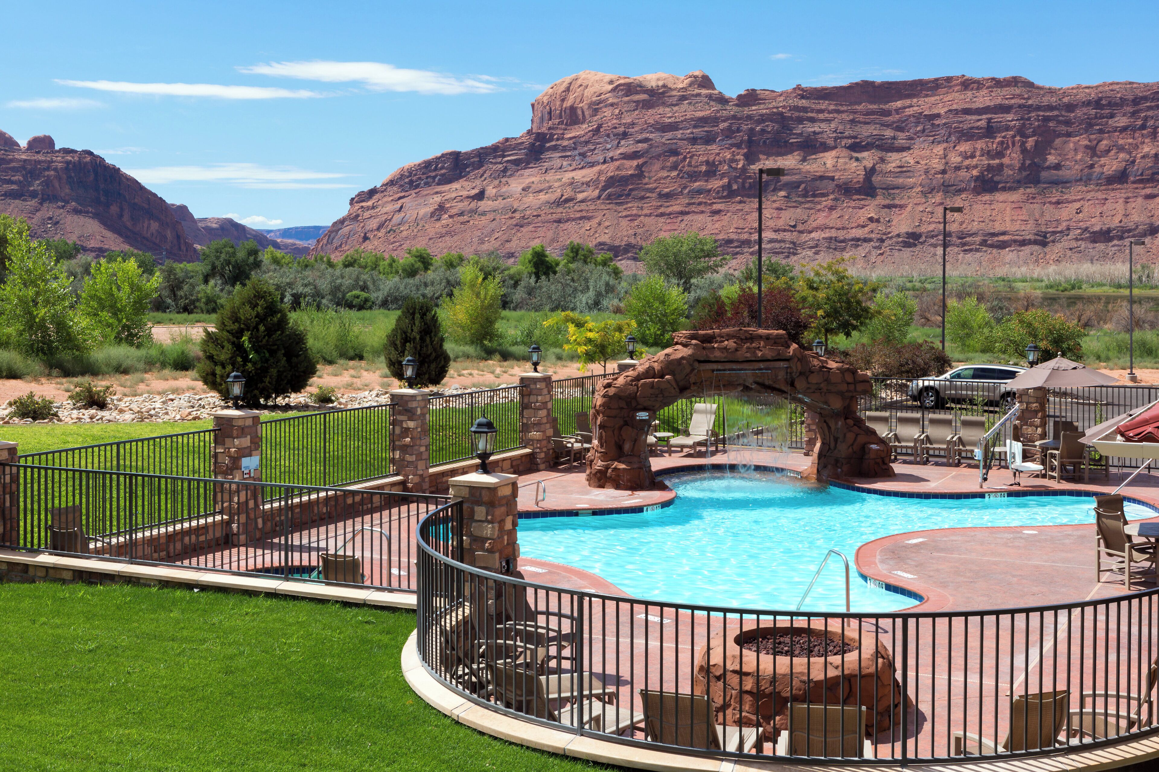 A swimming pool with a natural rock arch, surrounded by a fence, with a mountain backdrop.