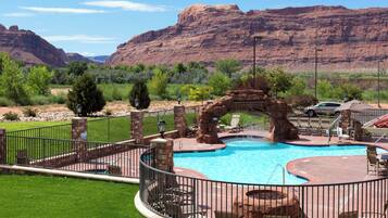 A swimming pool with a natural rock arch, surrounded by a fence, with a mountain backdrop.