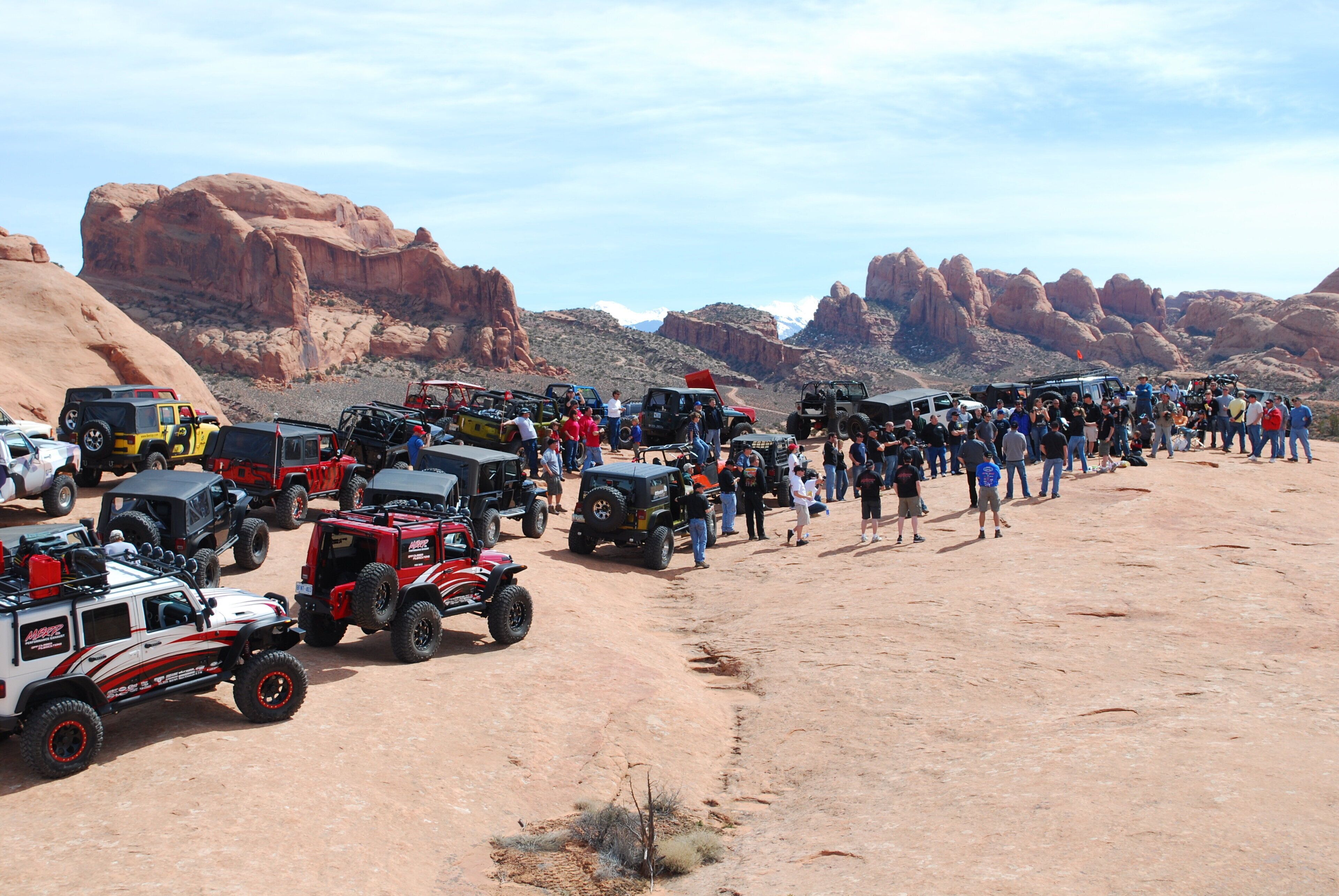A desert landscape with a group of off-road vehicles parked on a dirt road.