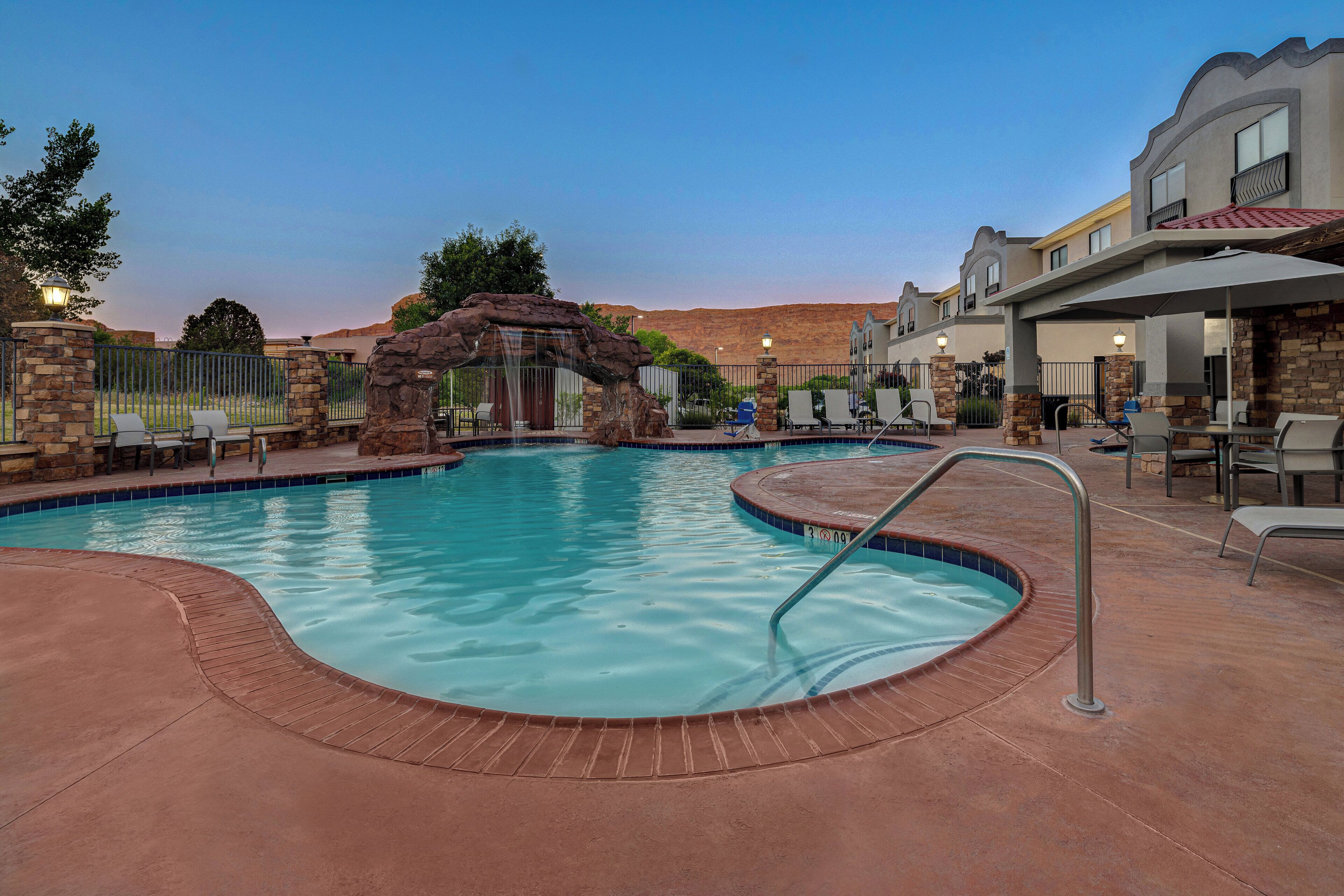 A swimming pool with a stone archway, lounge chairs, and a covered patio area.