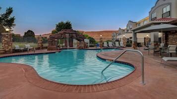 A swimming pool with a stone archway, lounge chairs, and a covered patio area.