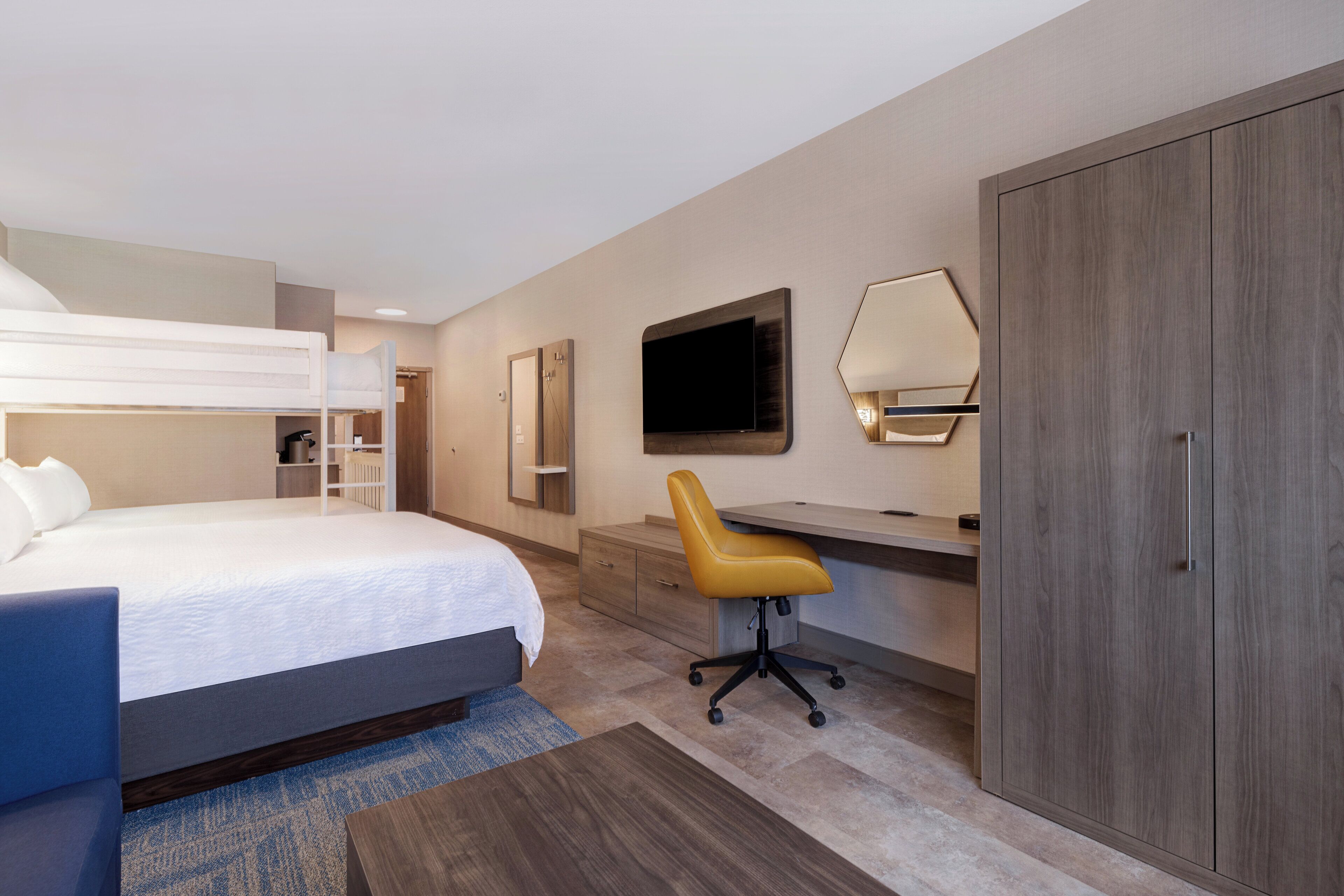 A hotel room with a bunk bed, a desk with a chair, a television, and a wardrobe.