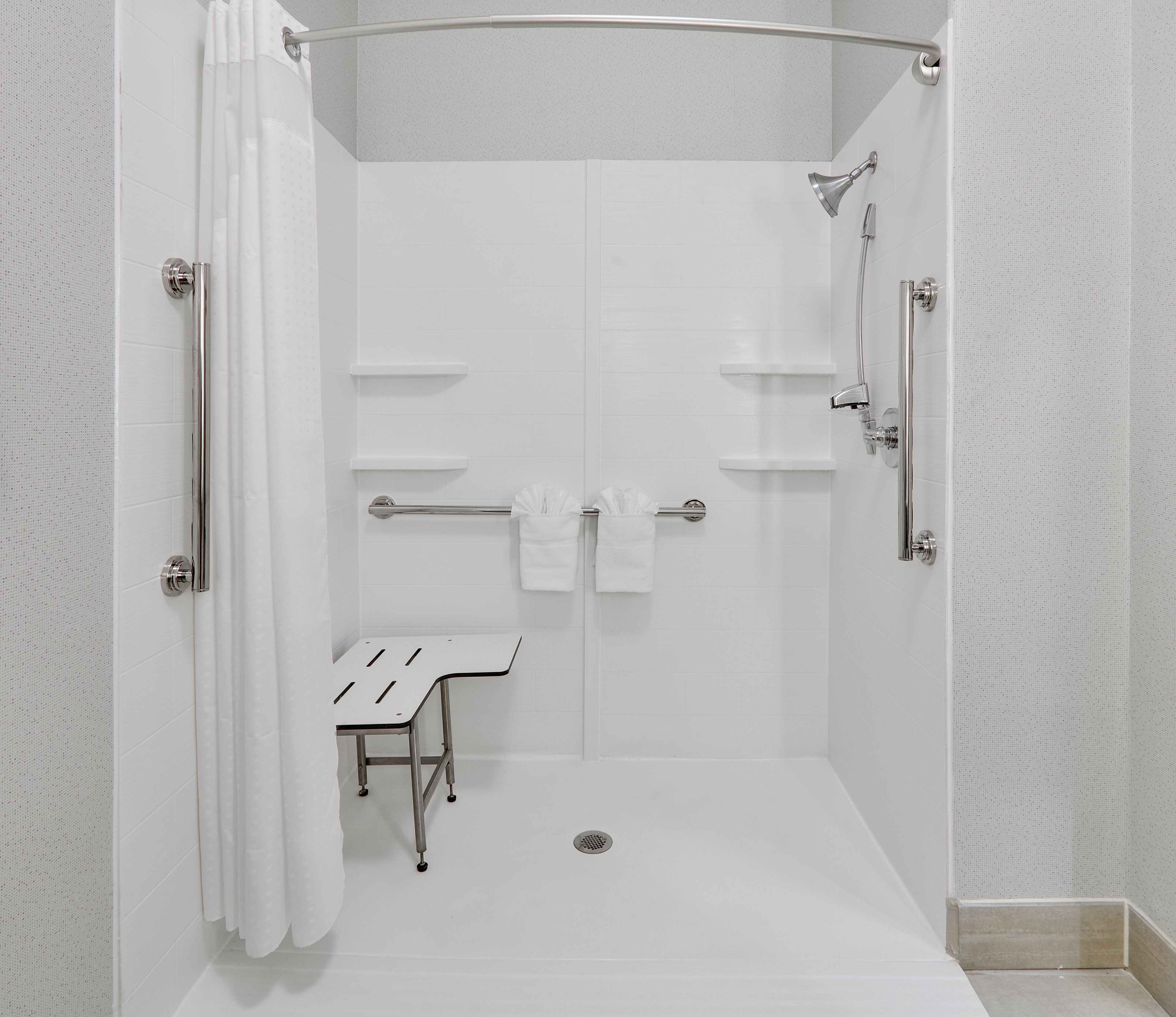 A modern shower area with a glass door, a bench, and a towel rack.