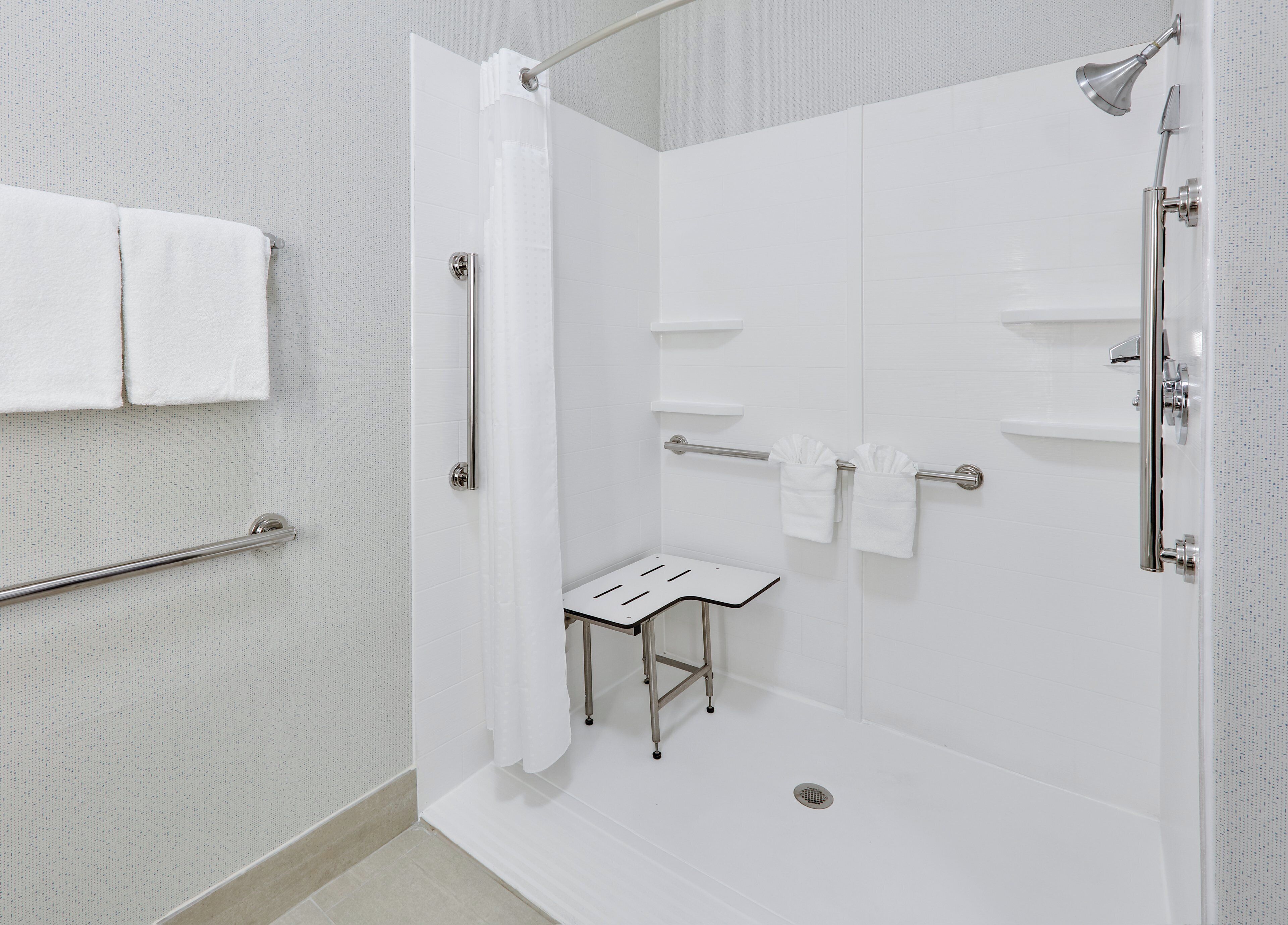 Ein modernes Badezimmer mit Dusche, Handtuchhalter und einer kleinen Sitzbank.