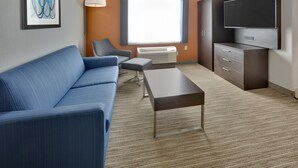A modern hotel room with a blue sofa, a small table, a chair, a TV, and a cabinet. - Holiday Inn Express Hotel & Suites Dallas - Duncanville by IHG (Duncanville)