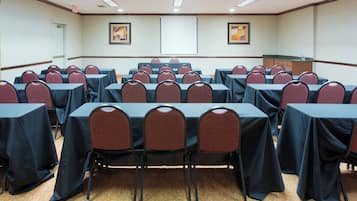 Une salle de conférence avec des rangées de tables et de chaises, un écran de projection et un sol recouvert de moquette.